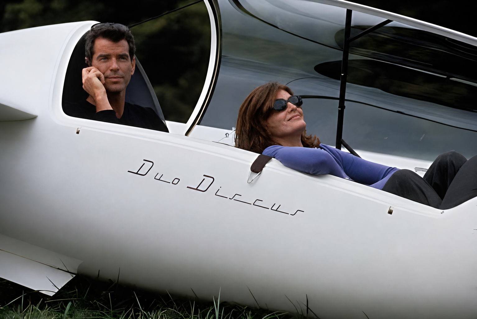 Two people seated in the cockpit of a white glider, close up