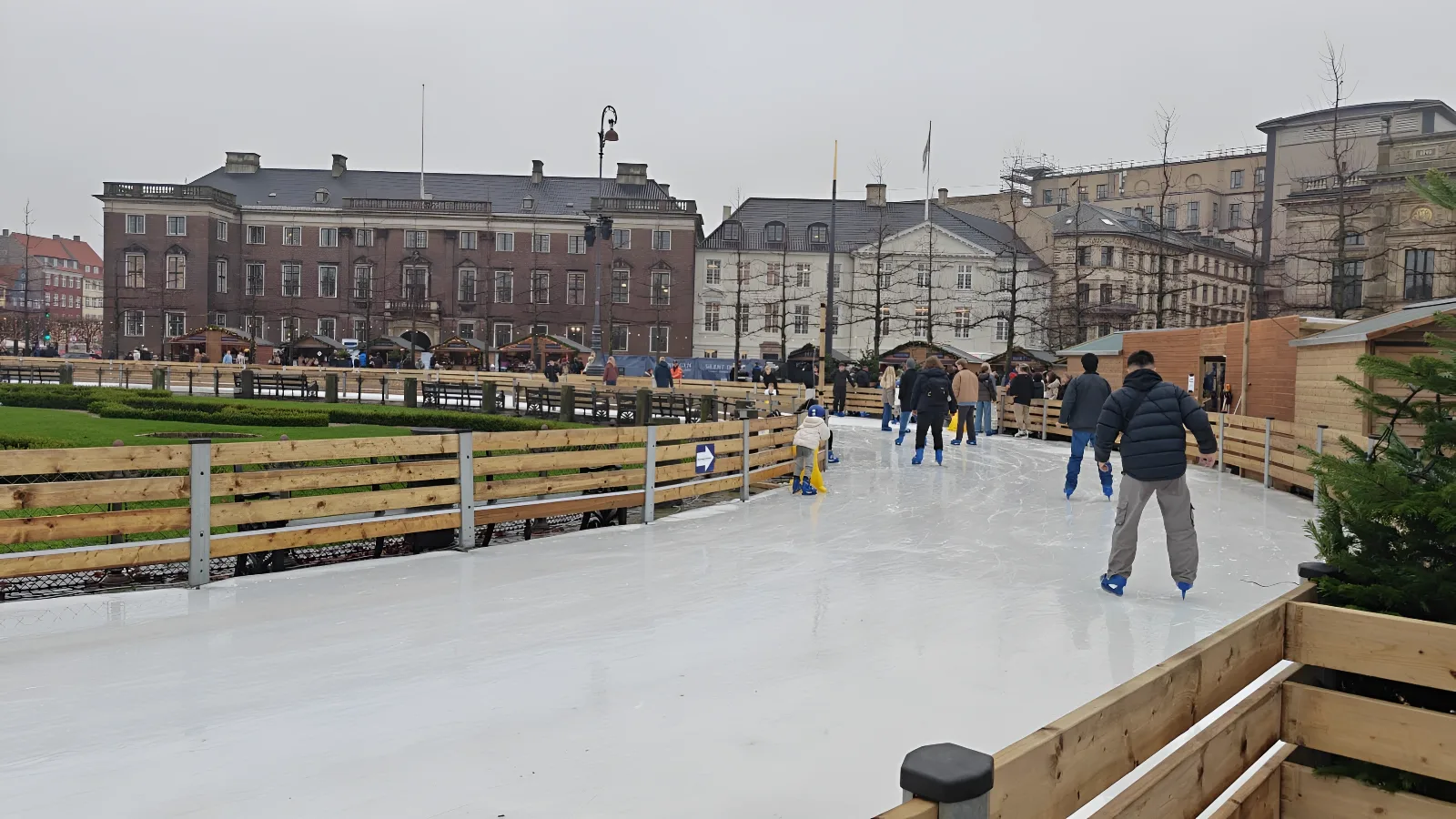 People ice skating outdoors in front of a Christmas market