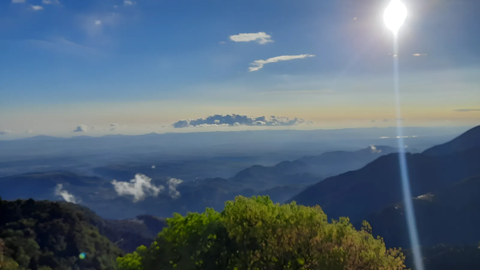 Sun flaring over layered, hazy mountain ridges